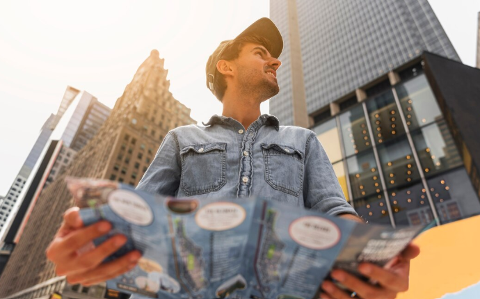 Hombre joven con gorra observando edificios altos mientras sostiene un plano analizando una ciudad moderna.
