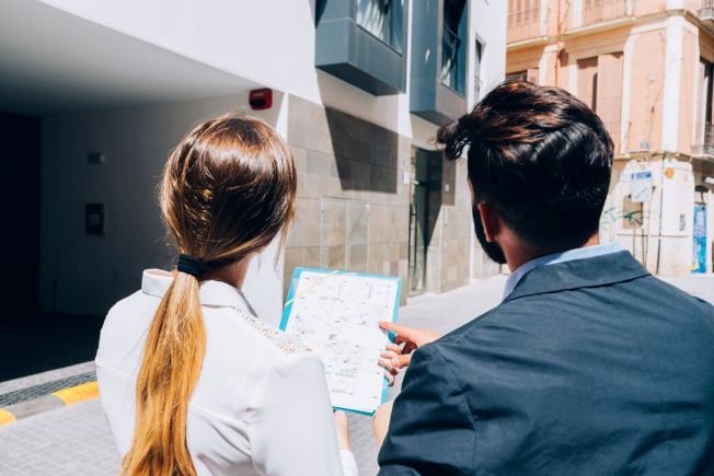 Dos personas observando un inmueble y revisando un plano urbano, analizando el diseño y distribución del proyecto